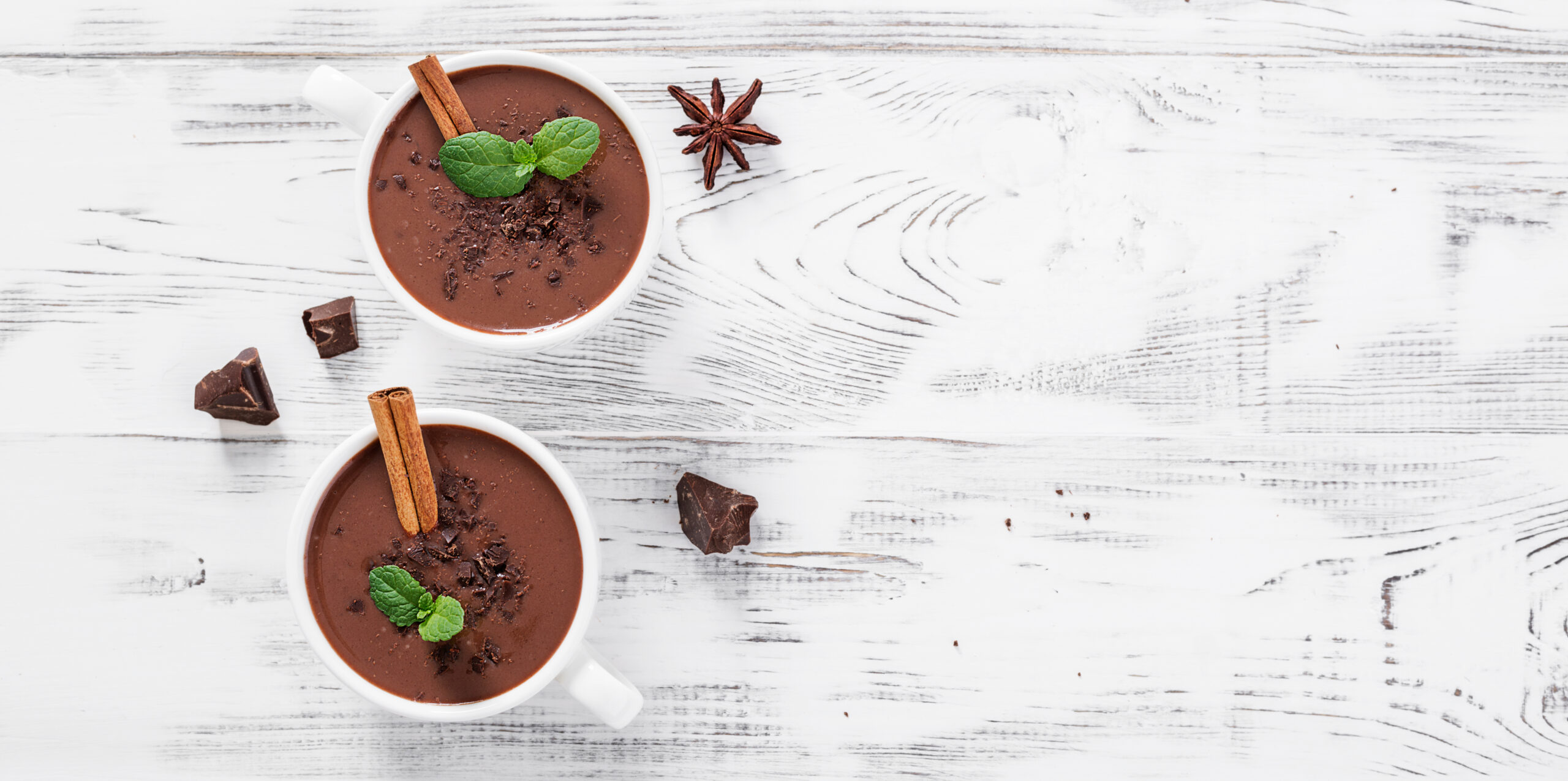 Hot chocolate drinks and chocolate pieces in white cup.